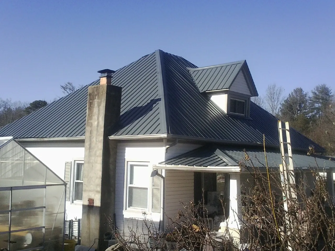 Dark blue standing seam metal roof on a white farmhouse with dormer — Slate & Tile Roof Repair by Roofing Brothers in Sawyer