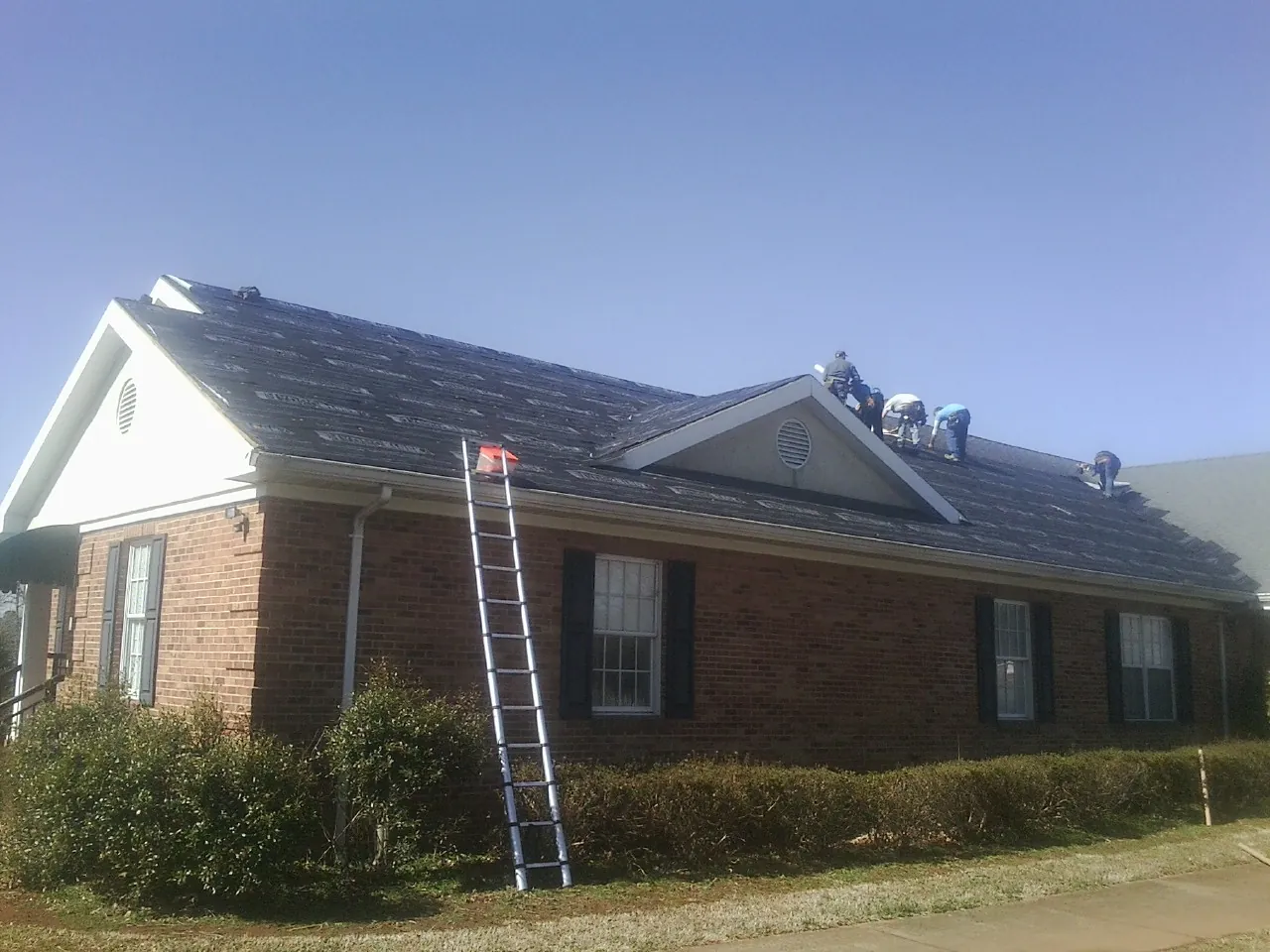 Crew tearing shingles off a brick ranch roof with a ladder set — Emergency Roof Repair work by our crew in Sawyer