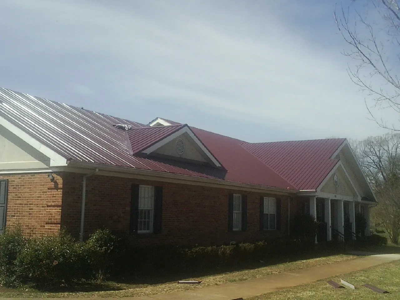 Red metal roof with gabled entries on a long brick building, from a Hail Damage Roof Repair job in Sawyer
