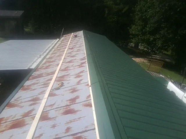 Old rusted panels beside newly installed green metal roofing — Wind Damage Roof Repair by Roofing Brothers in Sawyer