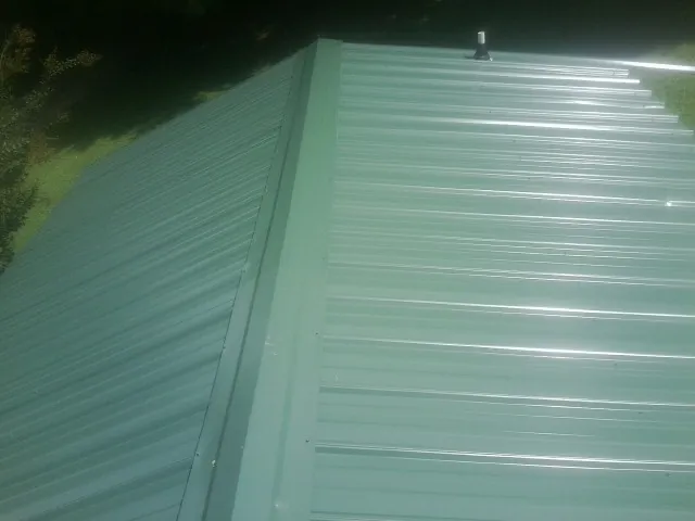 New green metal panels meeting at the ridge of a roof — Flat Roof Repair work by our crew in Sawyer