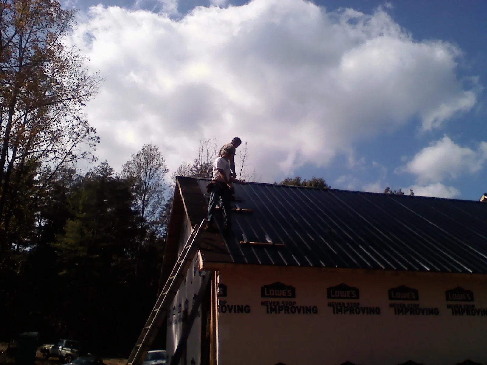 Roofer fastening dark metal panels high against a cloudy sky, from a Roof Inspection job in Sawyer