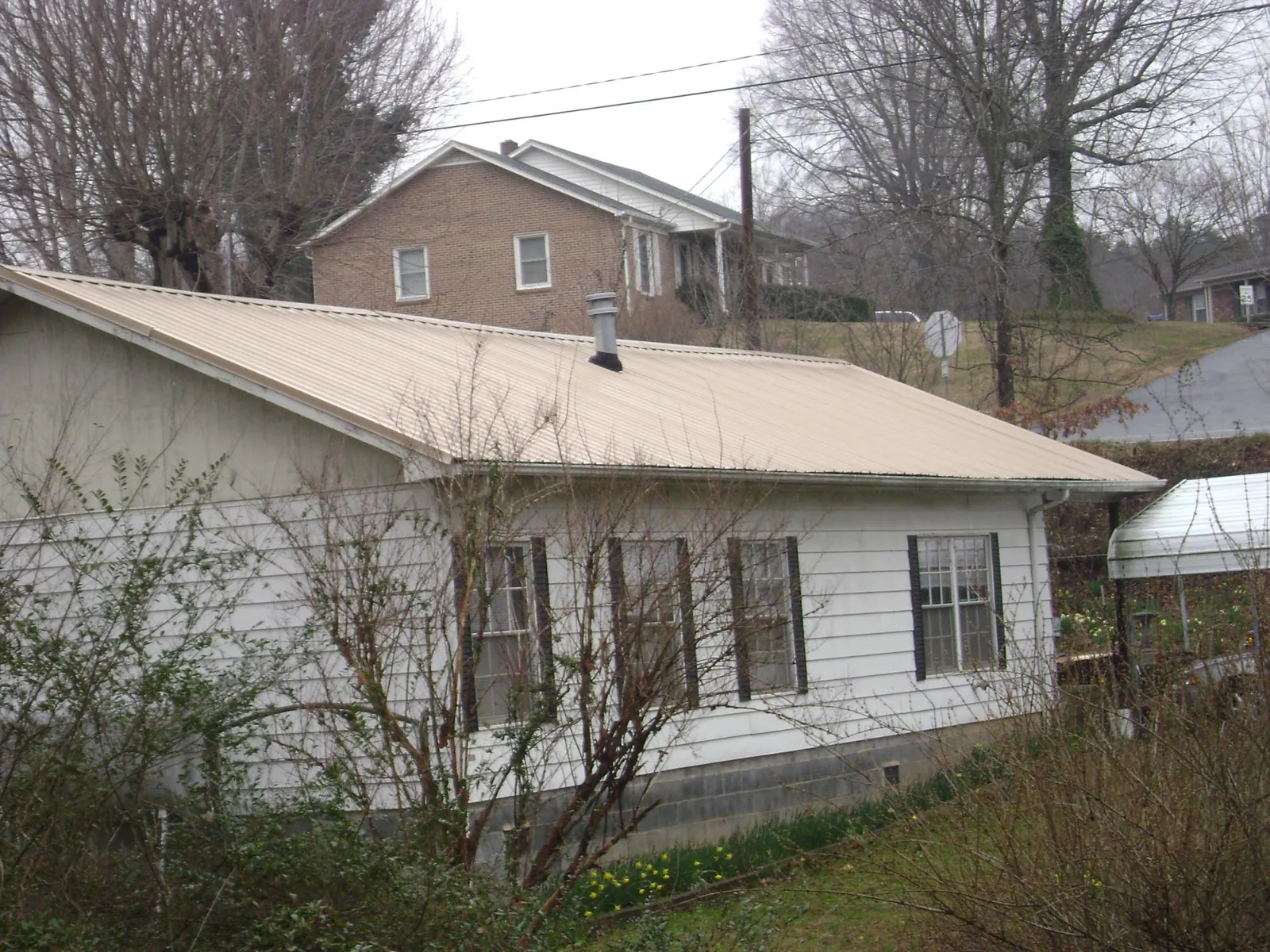 Tan metal roof on a white sided house set into a hillside — Commercial Roofing by Roofing Brothers in Sawyer