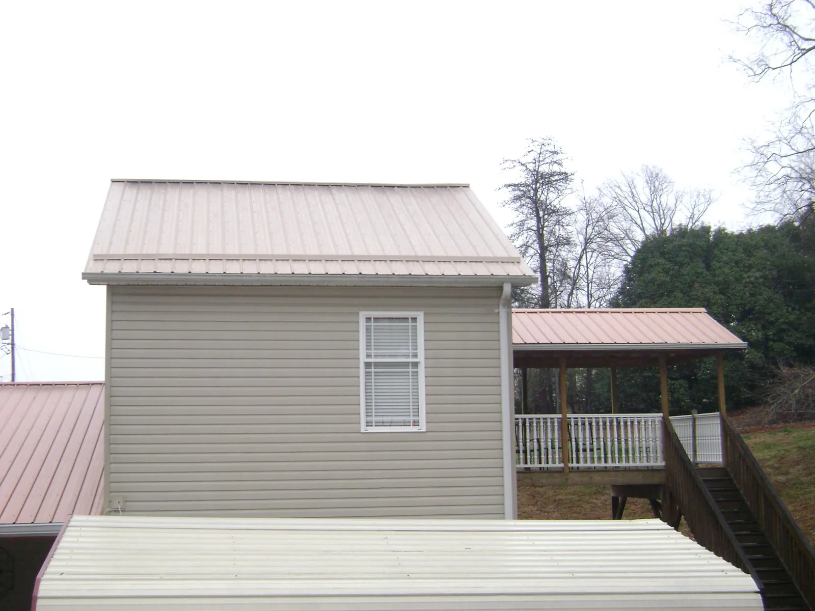 Tan metal roofs on a two story addition and attached porch, from a Roof Replacement job in Sawyer